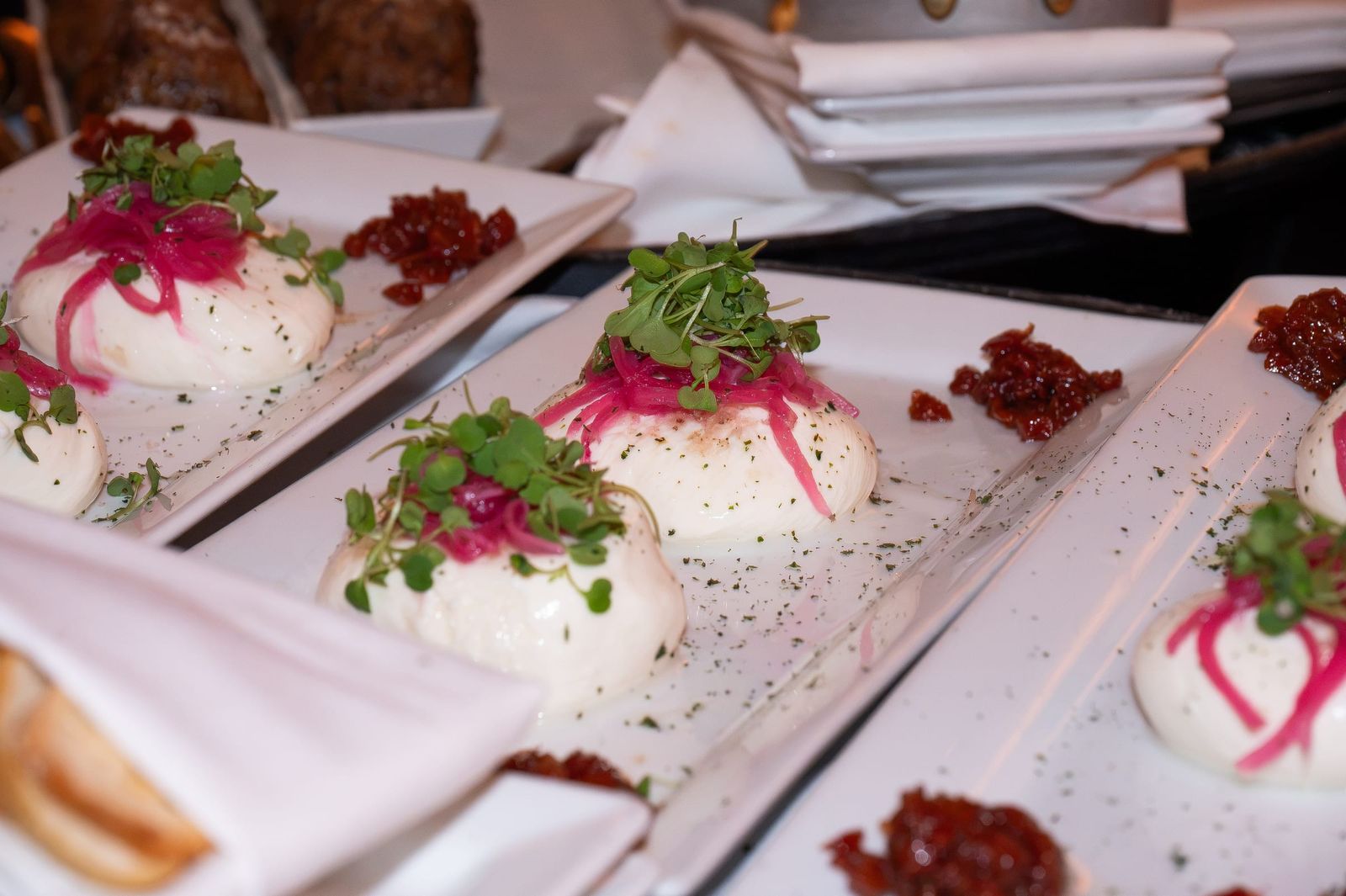 Burrata topped with pickled red onion and microgreens on long white plates.