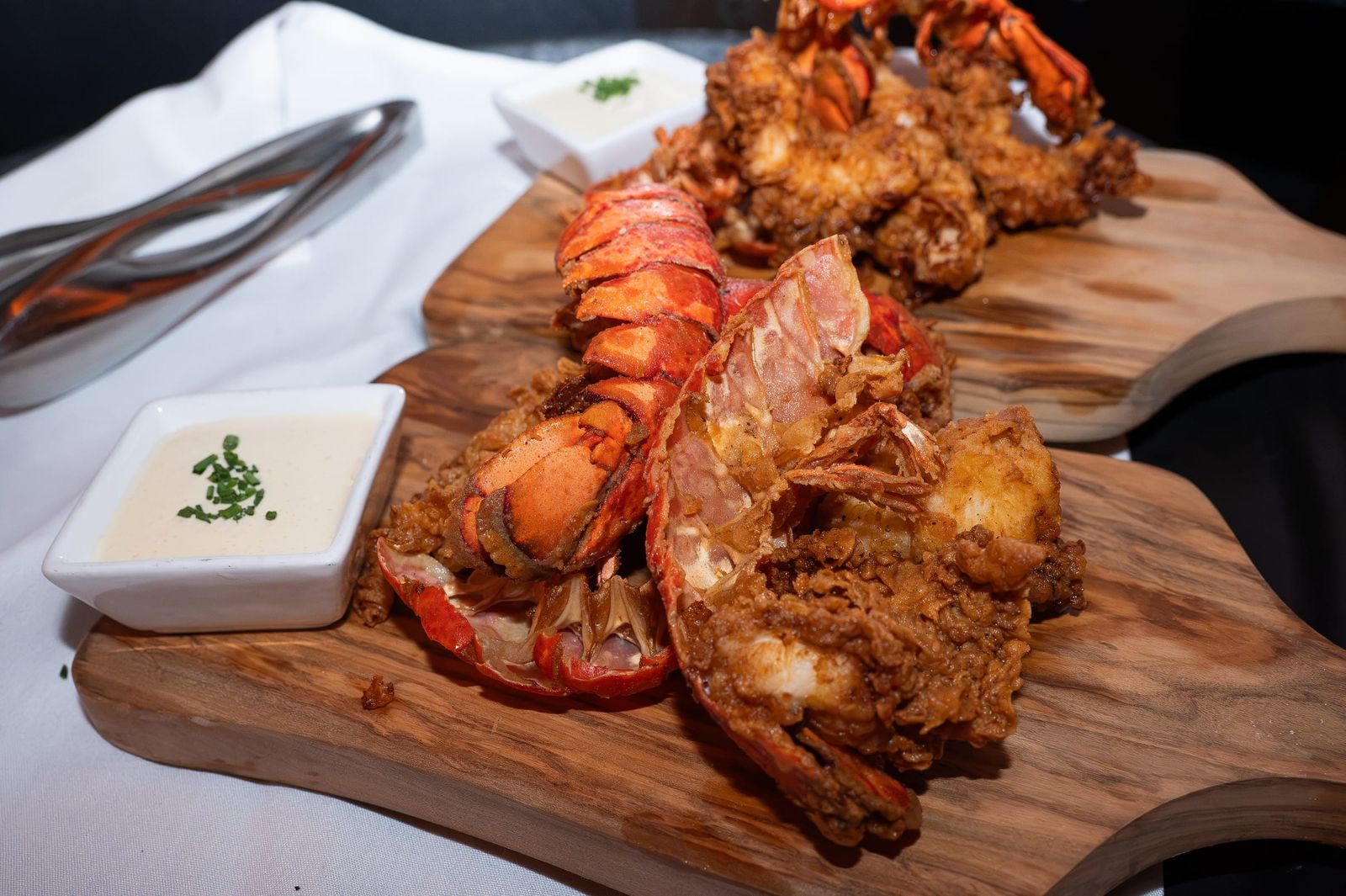 Crisp fried lobster tails on a wooden board with a dipping sauce.