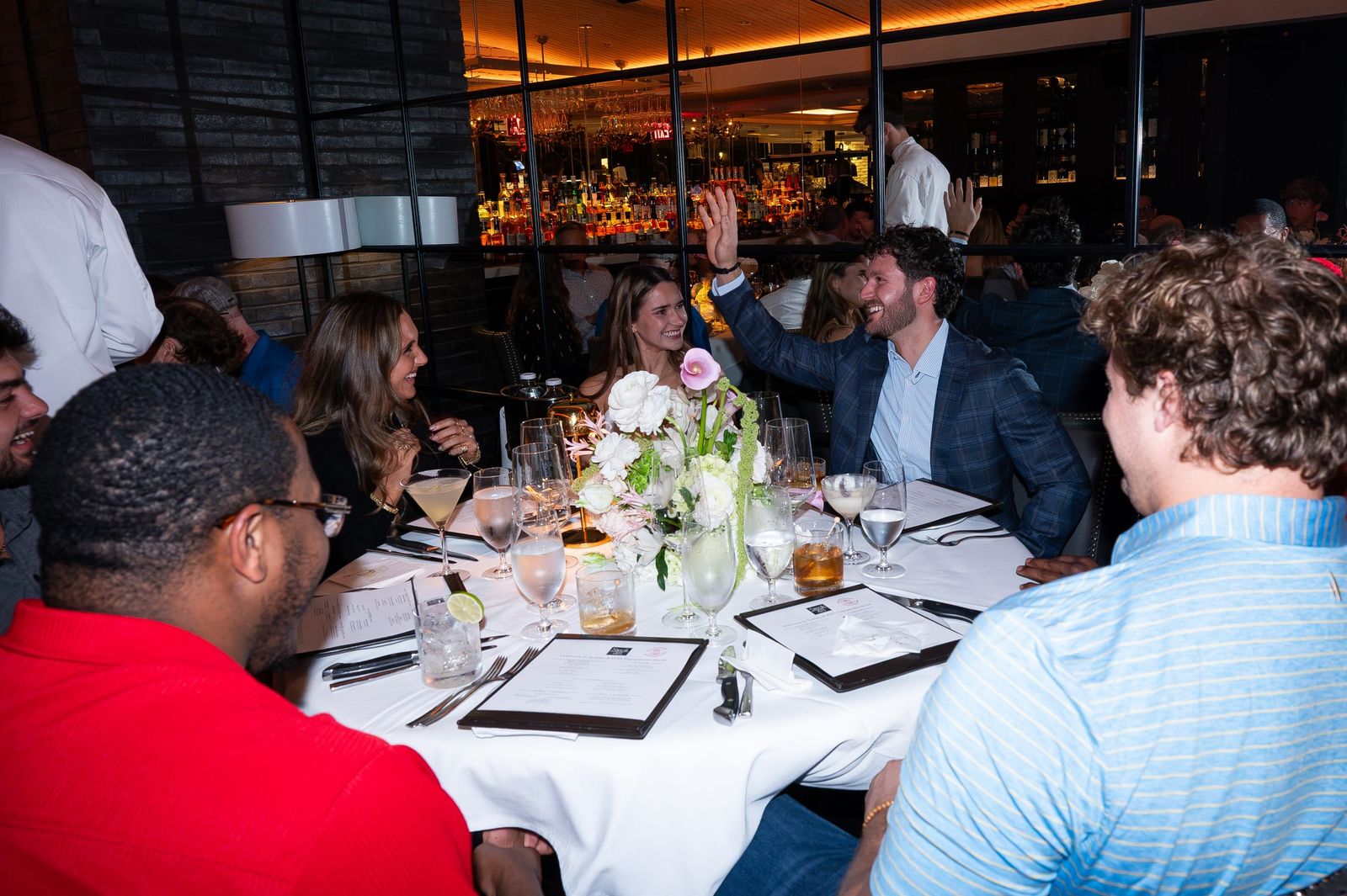 Guests laughing together around a round dinner table.