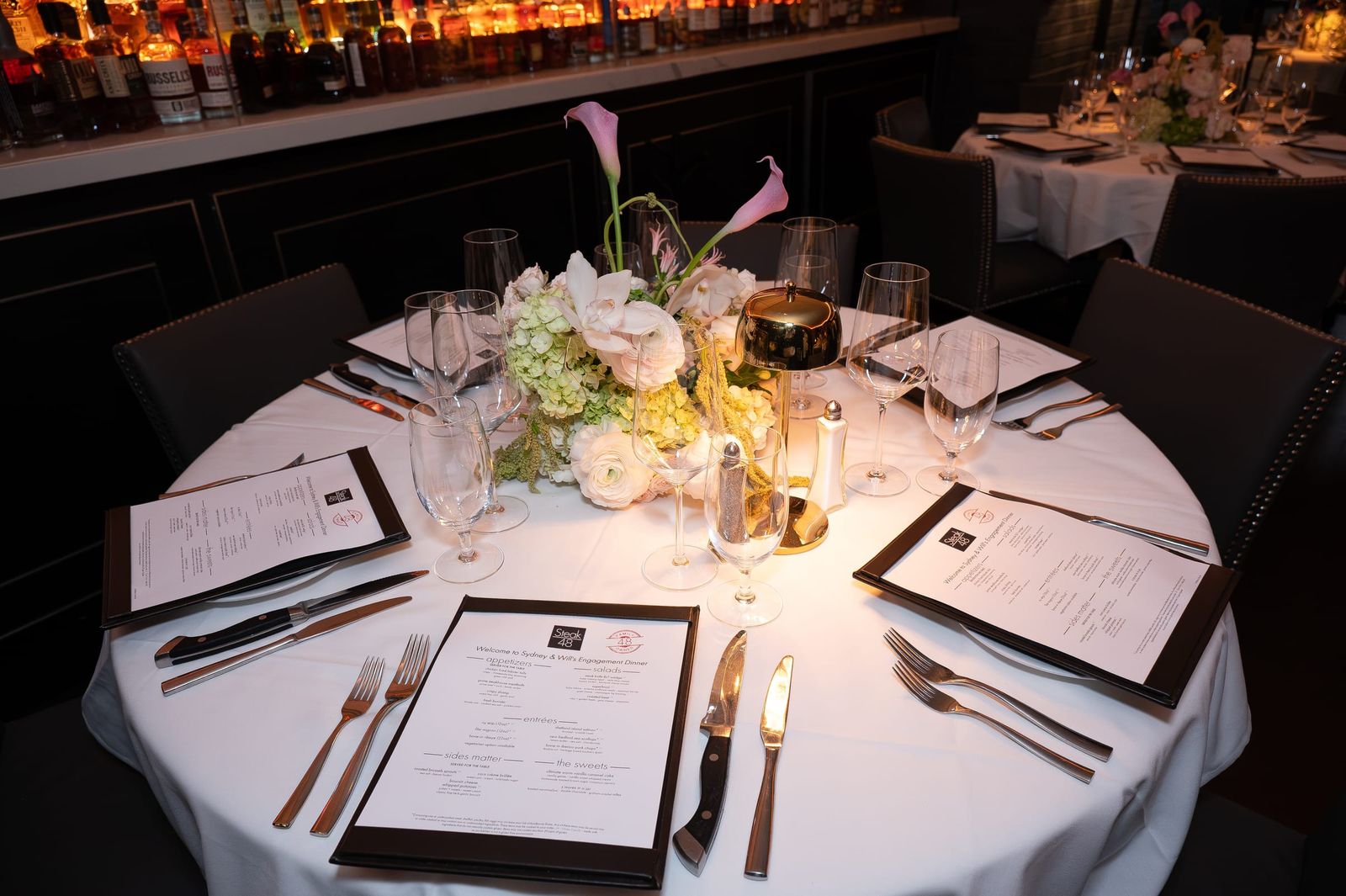 Place settings with printed menus, crystal glasses and a centerpiece of roses and calla lilies.