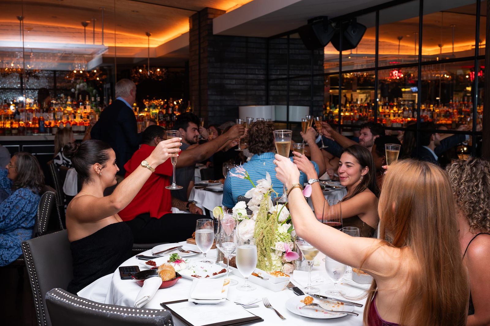 A dining room of guests raising their glasses for a toast.