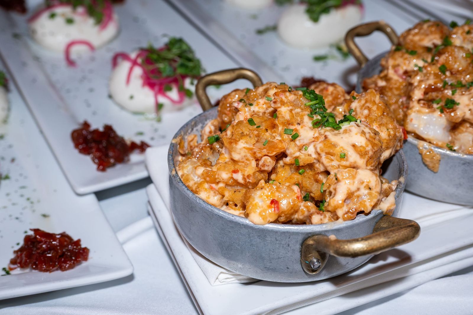 A golden seafood gratin in a small gold-handled pan, served beside burrata.
