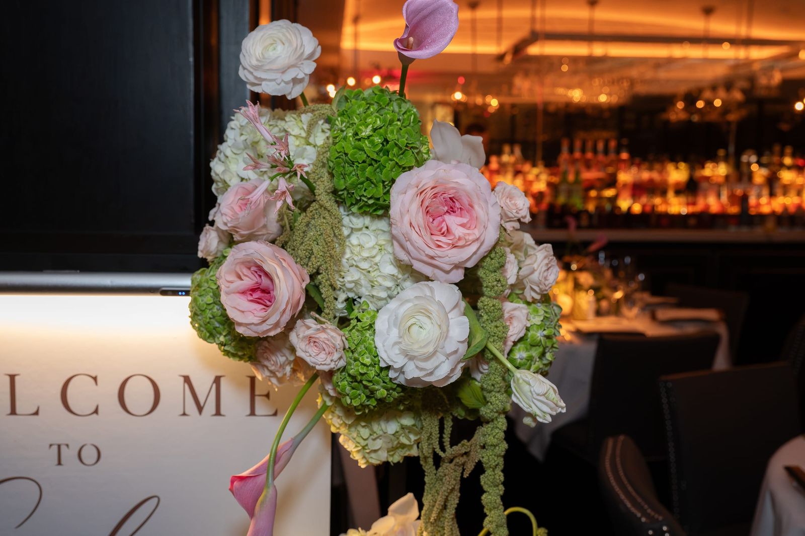 Blush garden roses, green hydrangea and calla lilies cascading beside a welcome sign.